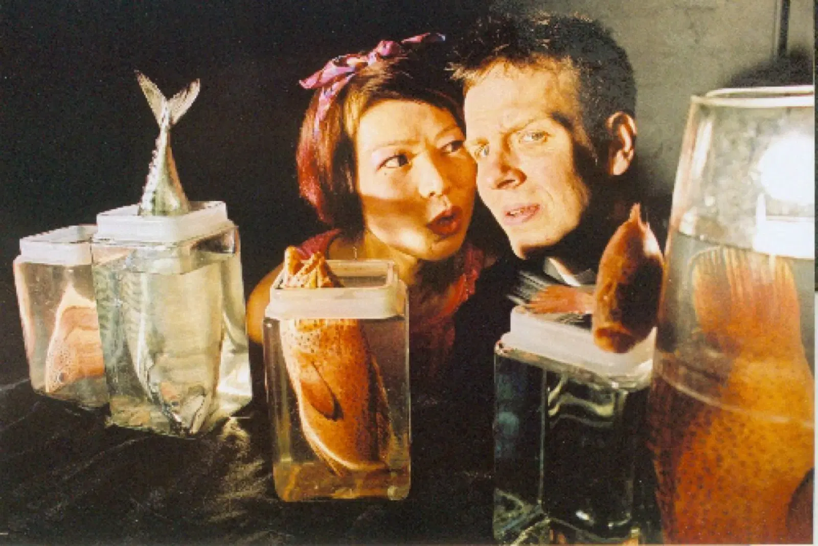 A couple making surprised and humorous faces at fish in transparent containers, evoking a sense of curiosity or playful interaction with marine life.